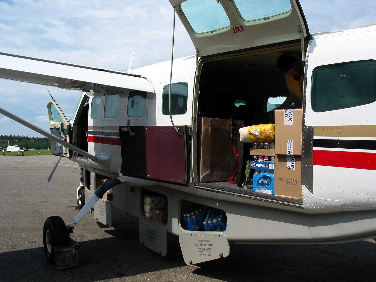 Carico visibile attraverso il portellone di un Cessna Caravan. Ogni collo contribuisce sia alla massa sia al momento: la posizione conta quanto il peso. Esempio visivo, non schema di caricamento.